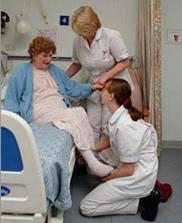 Two nurses helping an older lady from her hospital bed