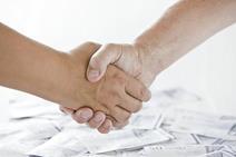 A handshake taking place above a pile of money
